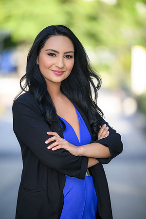 Professional outdoor portrait of a woman in a blue dress and black blazer with arms crossed.