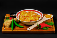 Food product photograph of seasoned raw chicken in a bowl with peppers, herbs, and spices on a wooden board.