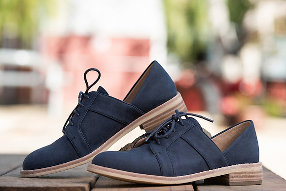 Commercial footwear photograph of navy lace-up shoes styled outdoors with a softly blurred background.