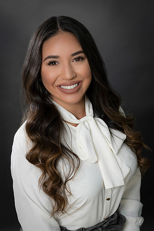 Professional studio headshot of a woman in a white blouse with a bow detail against dark gray.