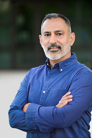 Professional outdoor portrait of a man in a blue button-down shirt with arms crossed.