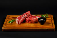 Food product photograph of raw beef steaks on a wooden cutting board with rosemary and seasoning.