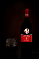 Studio product photograph of a Bellini Sangiovese bottle beside a glass of red wine on a reflective surface.