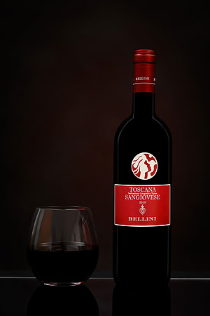 Studio product photograph of a Bellini Sangiovese bottle beside a glass of red wine on a reflective surface.