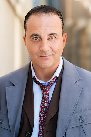 Professional portrait of a man in a gray suit with a loosened patterned tie and layered vest.