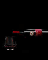 Commercial beverage photograph of a Bellini Sangiovese bottle pouring red wine into a glass on black.