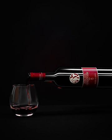 Commercial beverage photograph of a Bellini Sangiovese bottle pouring red wine into a glass on black.