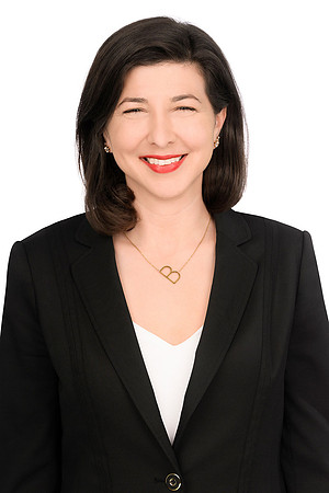 Clean studio business portrait of a smiling woman in a black blazer against white.