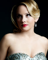 Close beauty portrait of a blonde woman in formal styling against a dark background.