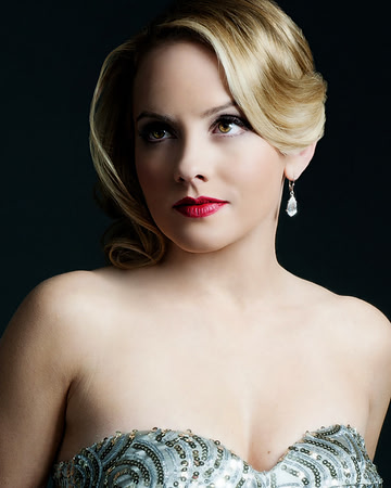 Close beauty portrait of a blonde woman in formal styling against a dark background.