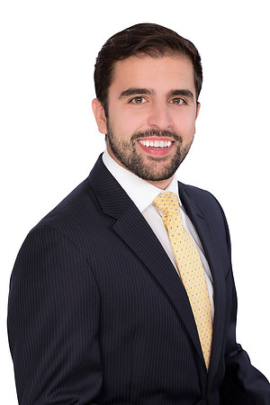 Professional studio portrait of a smiling man in a navy suit and yellow tie.