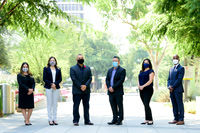 Group business portrait of six professionals standing outdoors while wearing face masks.