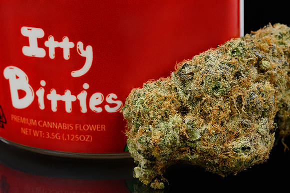Macro-style product photograph of a cannabis flower bud in front of red Itty Bitties packaging.