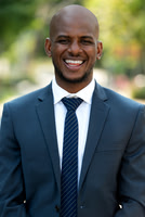 Professional outdoor headshot of a smiling man in a dark suit and striped tie.