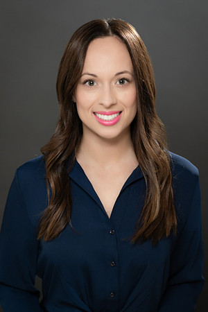 Professional studio headshot of a smiling woman in a navy blouse against dark gray.